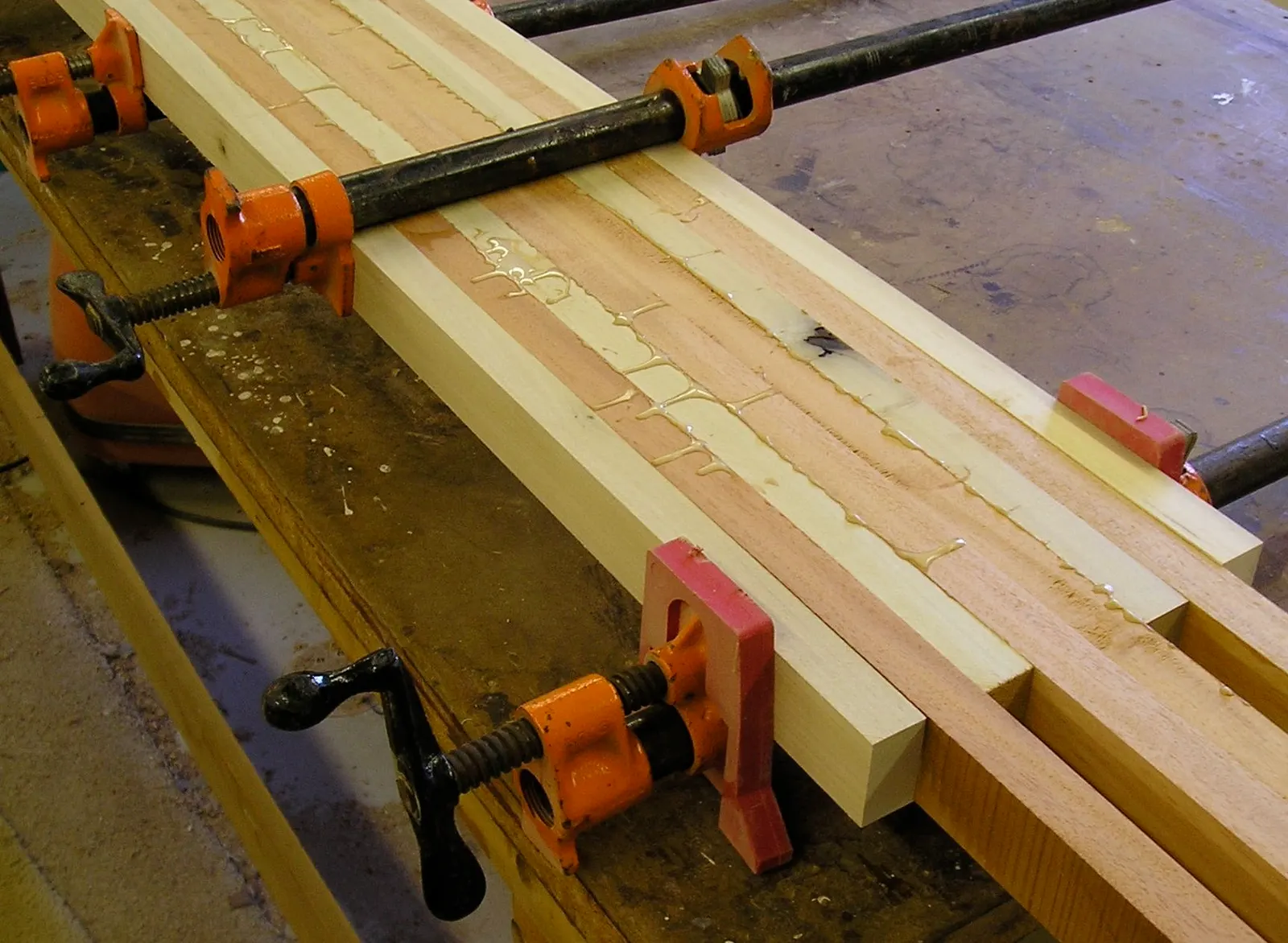 Boards glued up edge to edge, held in orange pipe clamps.