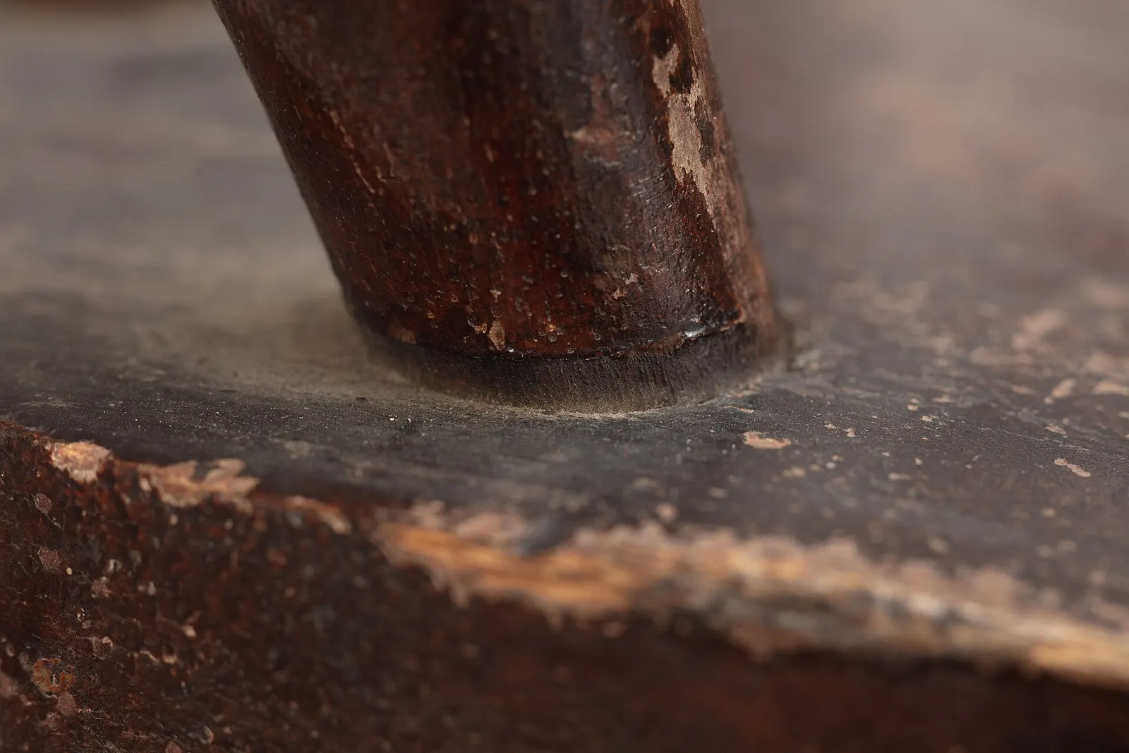 Close-up of a worn wooden chair leg standing on a dark floor.