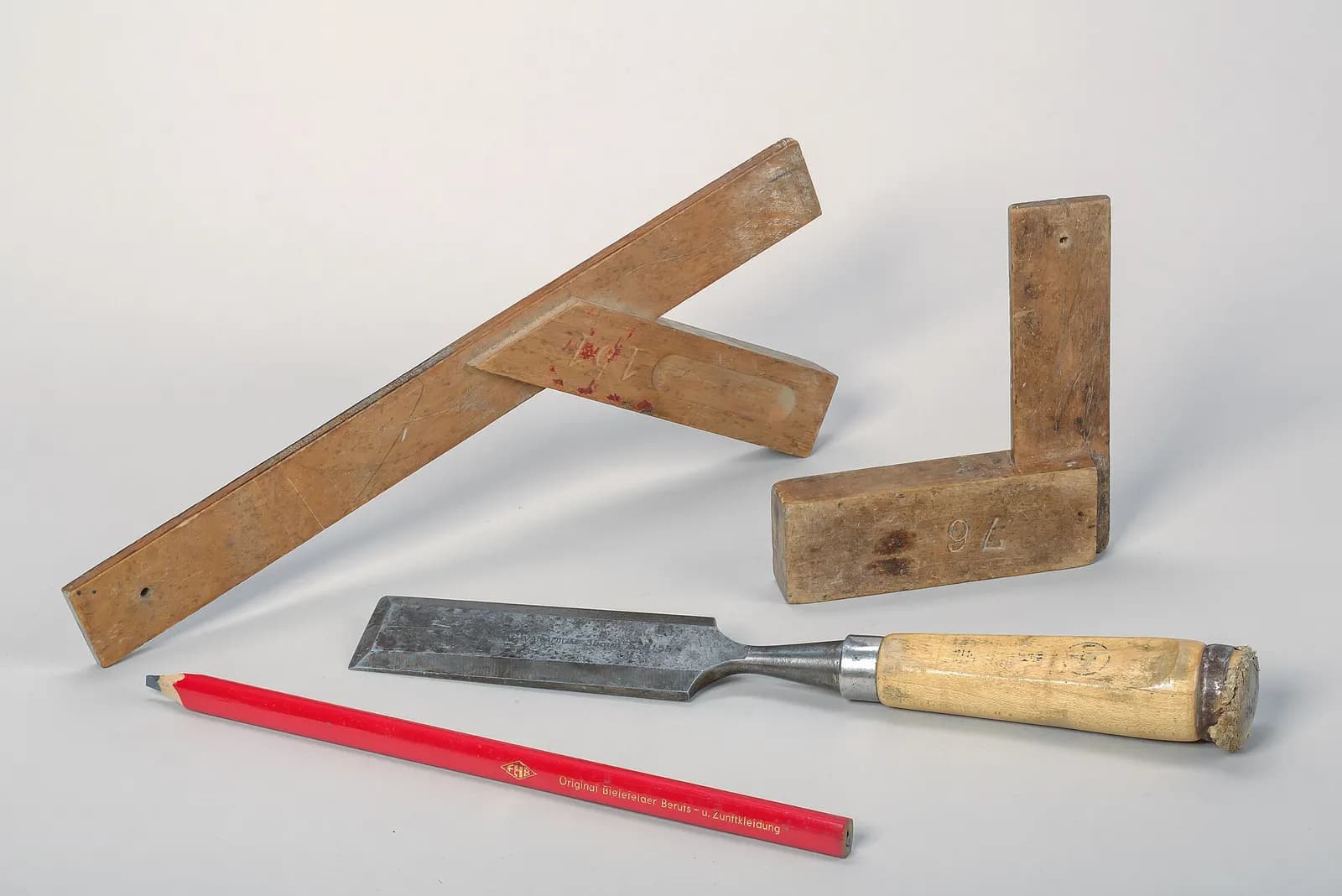 A chisel, a try square and a red carpenter's pencil laid on a table.