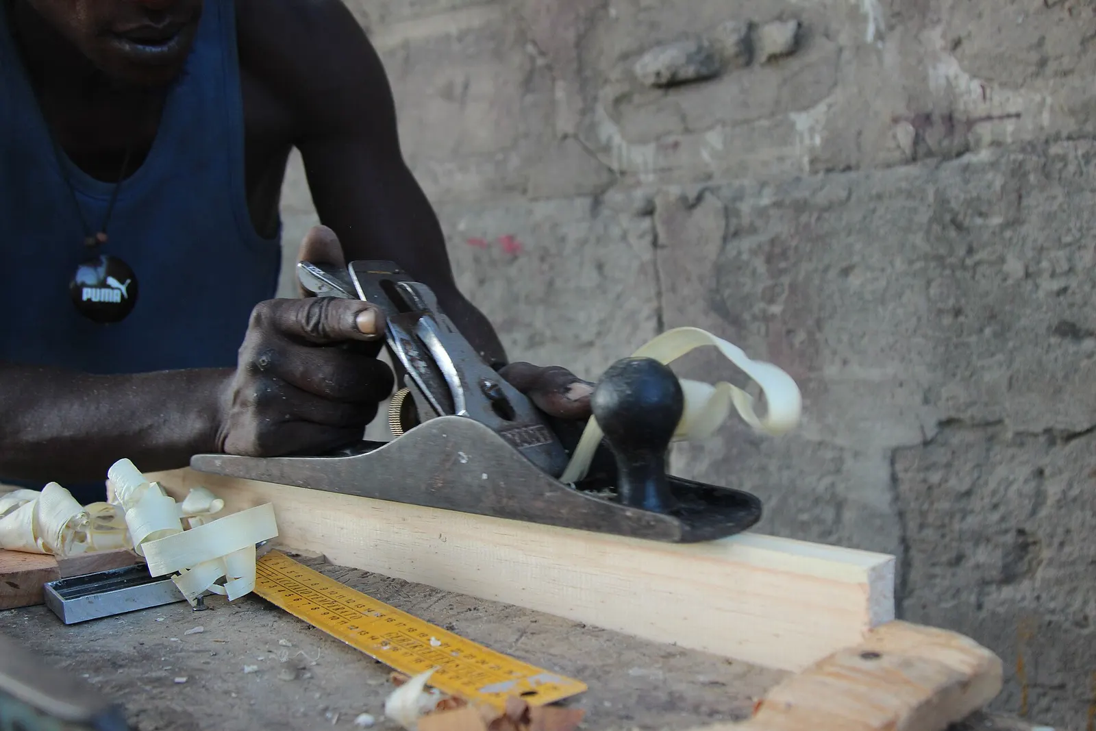 Hands pushing a hand plane along a board, shavings curling off.