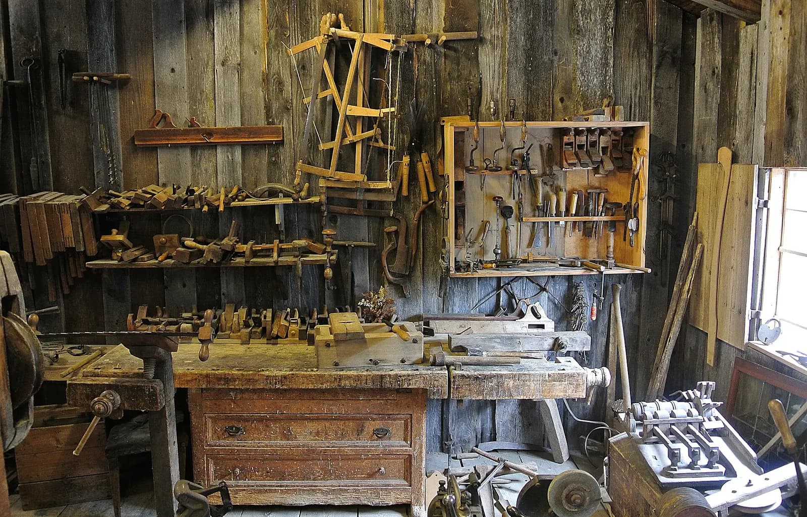 A woodworking workshop: hand tools racked on the wall above a timber workbench.